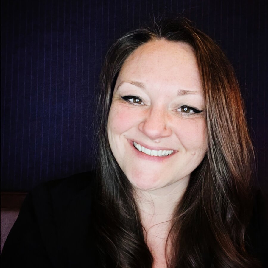 Amanda Baker, smiling, with long brown hair, in a dark jacket against a deep blue background